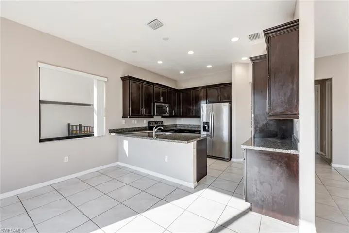 Kitchen featuring dark stone counters, kitchen peninsula, appliances with stainless steel finishes, light tile patterned floors, and dark brown cabinetry