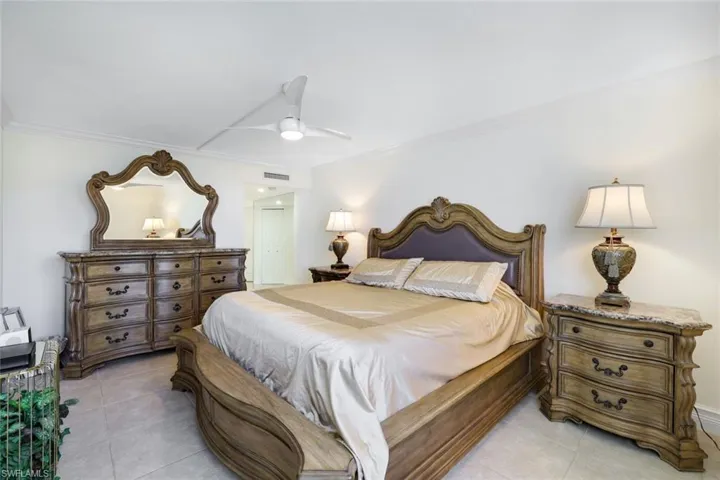 Bedroom with light tile patterned floors, ornamental molding, and ceiling fan