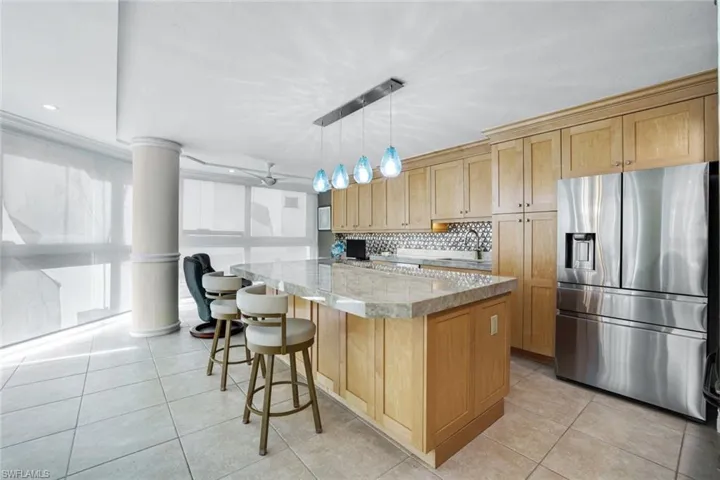 Kitchen featuring stainless steel fridge, decorative light fixtures, backsplash, a center island, and light stone countertops
