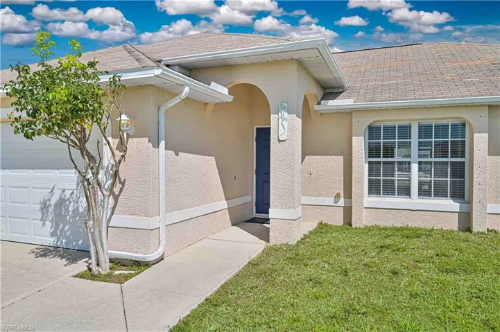 View of exterior entry with stucco siding, an attached garage, a yard, and roof with shingles