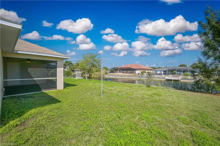 View of green lawn featuring a water view, a sunroom, and a ceiling fan