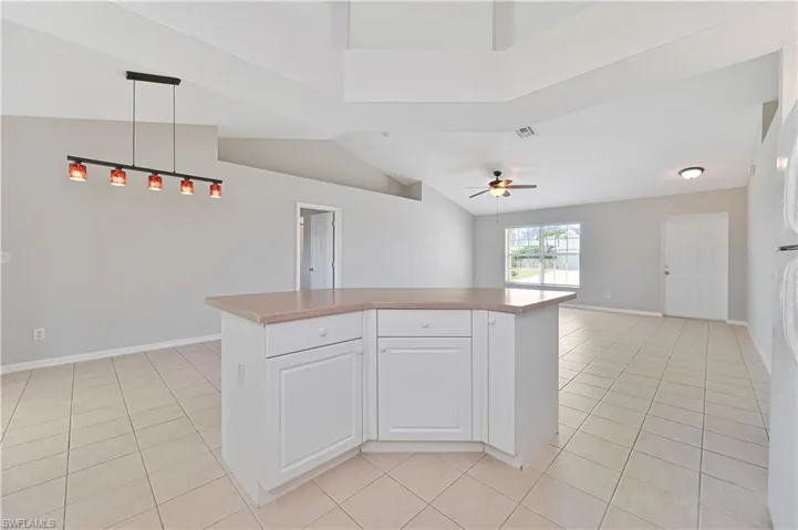 Kitchen featuring white cabinetry, light tile patterned floors, open floor plan, decorative light fixtures, and lofted ceiling