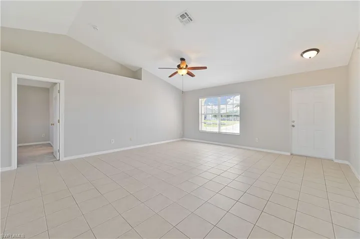 Empty room featuring ceiling fan, vaulted ceiling, and light tile patterned floors