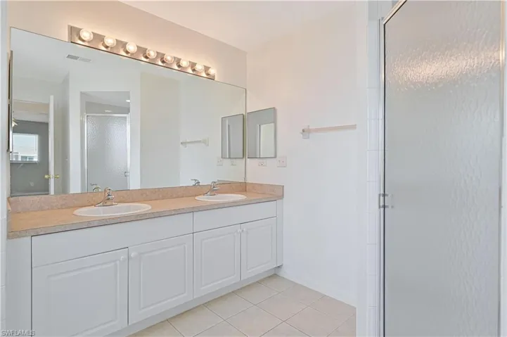Full bathroom with double vanity, a shower stall, and light tile patterned floors