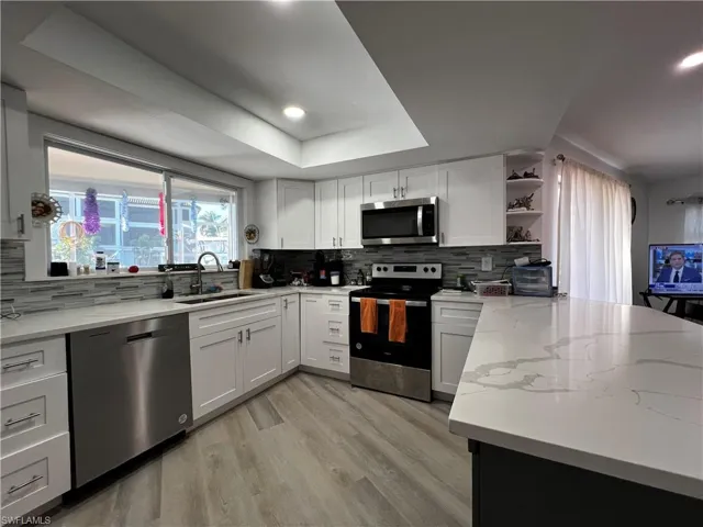 Kitchen with sink, appliances with stainless steel finishes, a raised ceiling, and backsplash
