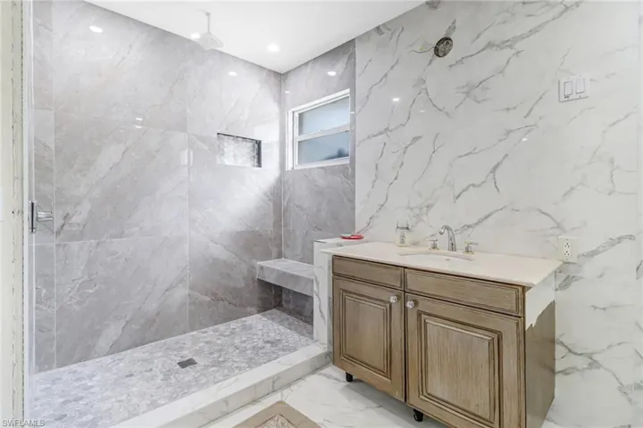 Bathroom with tile walls, a tile shower, tile flooring, and vanity