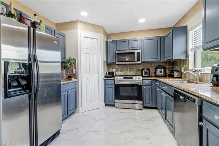 Kitchen featuring light stone countertops, stainless steel appliances, backsplash, sink, and light tile floors