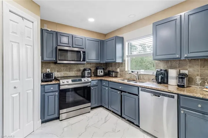Kitchen with tasteful backsplash, light tile flooring, light stone counters, sink, and appliances with stainless steel finishes