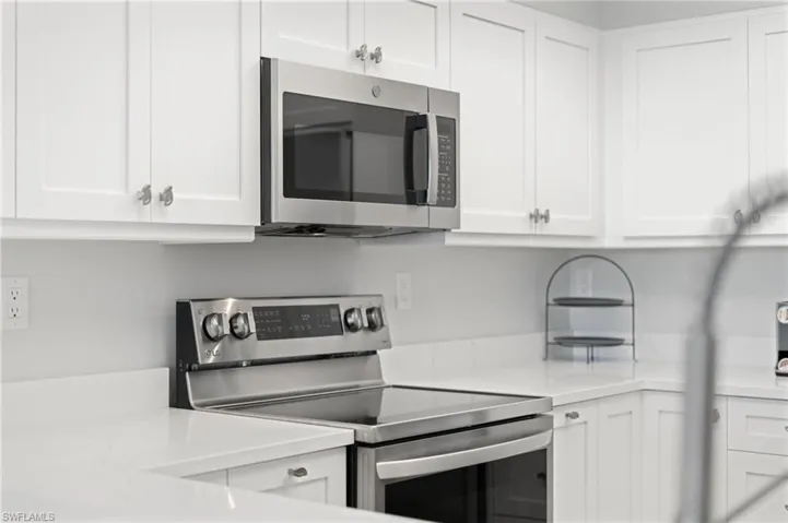 Kitchen with stainless steel appliances, white cabinets, and light stone countertops