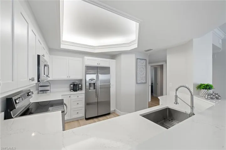 Kitchen with appliances with stainless steel finishes, light wood-style flooring, white cabinets, and light stone counters