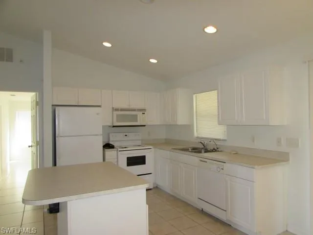 Kitchen featuring white appliances, vaulted ceiling, recessed lighting, white cabinets, and light countertops