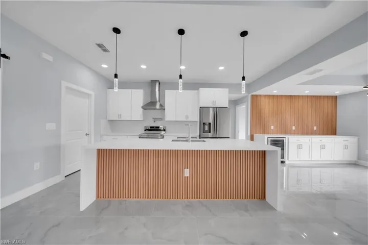 Kitchen with a large island, white cabinets, decorative light fixtures, and light stone counters