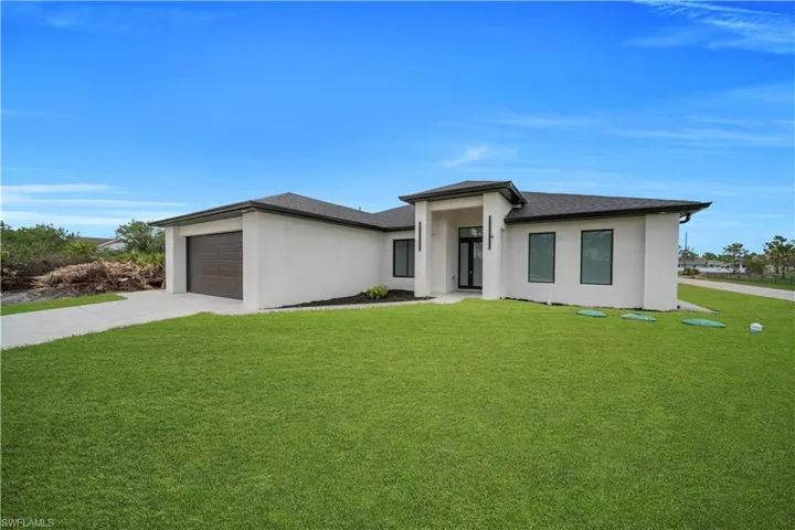 Prairie-style home featuring stucco siding, a front lawn, driveway, and a shingled roof
