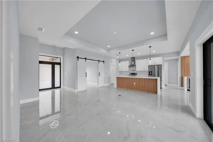 Unfurnished living room with a barn door, a tray ceiling, recessed lighting, and light marble finish floors