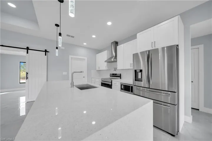 Kitchen with a barn door, stainless steel appliances, white cabinetry, and light stone counters