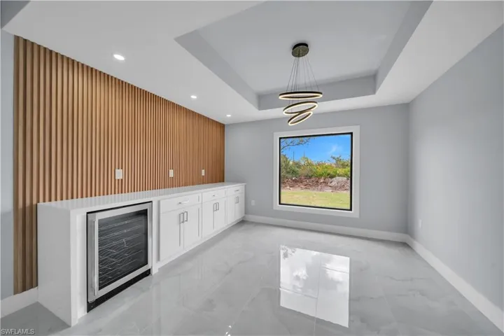 Bar with white cabinets, beverage cooler, an accent wall, wood walls, and light marble finish floors