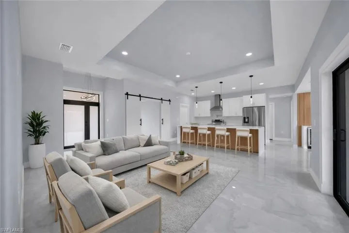 Living area featuring a barn door, a tray ceiling, recessed lighting, and light marble finish flooring