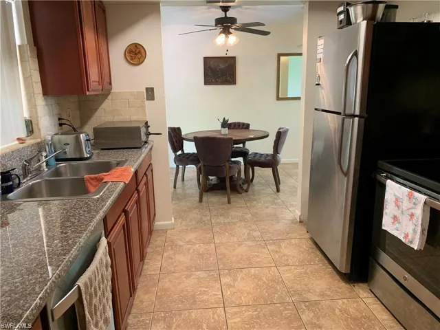 Kitchen featuring stainless steel appliances, ceiling fan, tasteful backsplash, light tile patterned floors, and wood finish cabinets