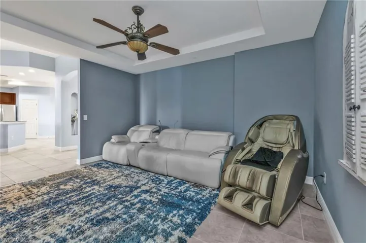 Living room with a ceiling fan, a raised ceiling, baseboards, and light tile patterned floors
