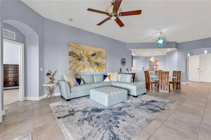 Tiled living room featuring arched walkways, ceiling fan with notable chandelier, visible vents, and baseboards