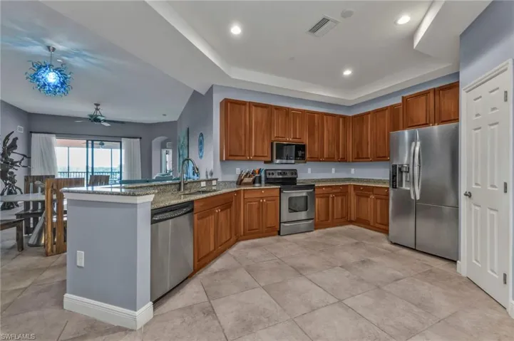 Kitchen with stainless steel appliances, a raised ceiling, brown cabinetry, a sink, and a peninsula