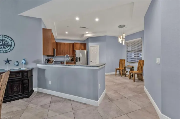 Kitchen featuring a peninsula, baseboards, stainless steel fridge with ice dispenser, dark stone counters, and brown cabinetry