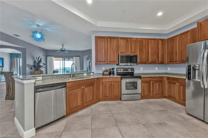 Kitchen featuring arched walkways, stainless steel appliances, brown cabinetry, a sink, and a peninsula