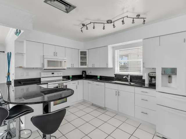Kitchen with white appliances, dark countertops, a sink, and white cabinetry
