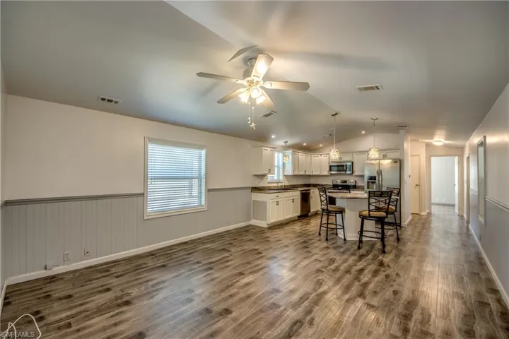 Spacious open-concept living area featuring wood-look flooring, a ceiling fan, and a kitchen with white cabinetry, stainless steel appliances, and an island with seating