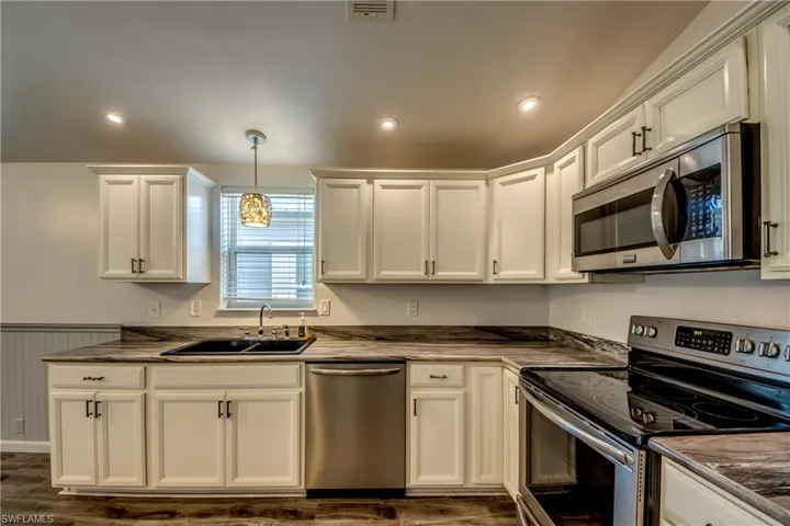 The kitchen features white cabinetry, dark countertops, a stainless steel microwave, a stainless steel dishwasher, and a black sink