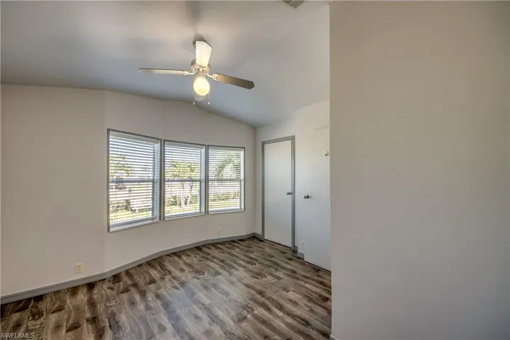 This room features wood-look flooring, a vaulted ceiling with a ceiling fan, and a trio of windows offering exterior views