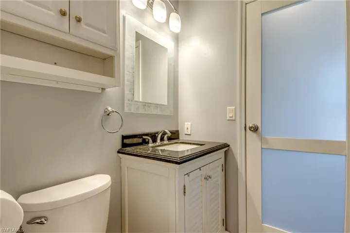 This bathroom features a vanity with a dark countertop and a wall-mounted mirror with overhead lighting