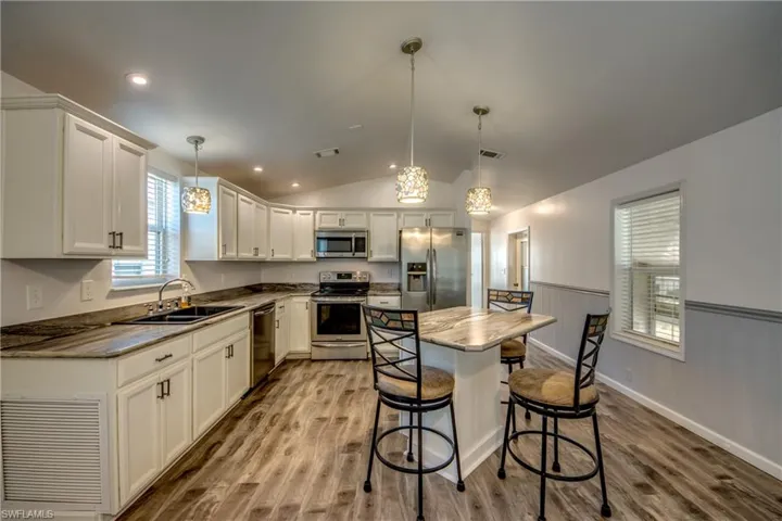The kitchen features white cabinetry, stainless steel appliances, and a central island with a countertop and seating