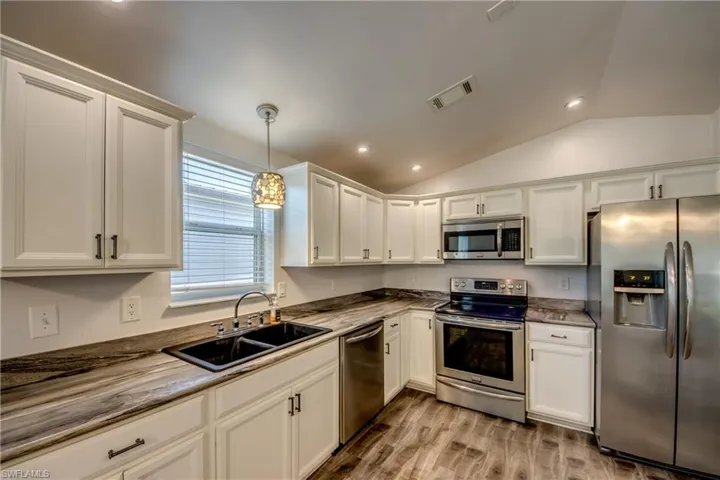 Well-appointed kitchen featuring white cabinetry, stainless steel appliances, a double basin sink, and wood-look flooring