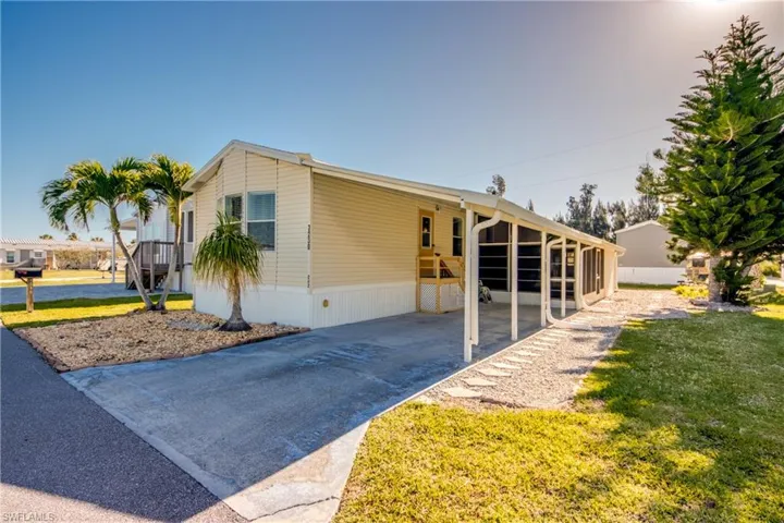 The property features a concrete driveway, a screened-in porch, and a landscaped yard with mature trees and palm trees