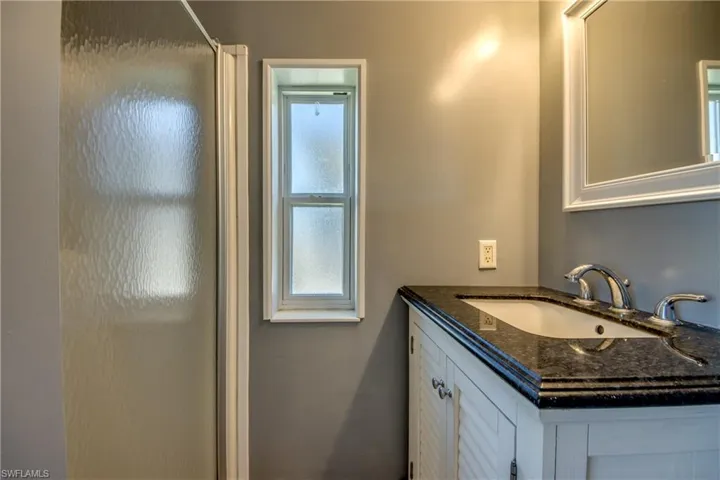 Bathroom with a shower enclosure, a window, and a vanity featuring a dark countertop, white sink, and chrome fixtures