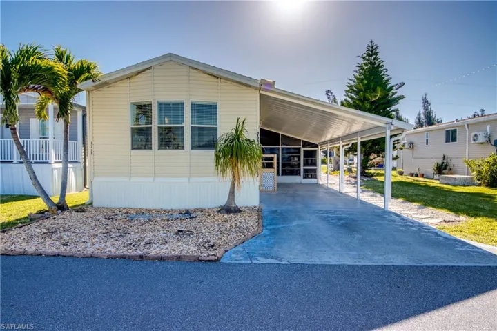 The property features a carport, a rock garden with palm trees, and light-colored siding