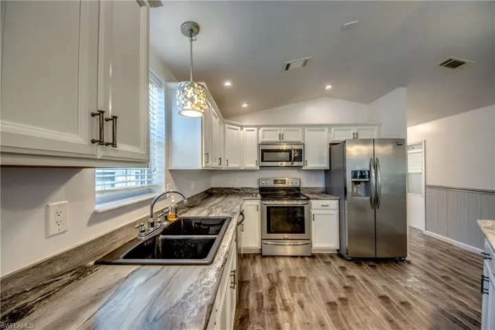 The kitchen features white cabinetry with dark hardware, a dark double basin sink, and stainless steel appliances