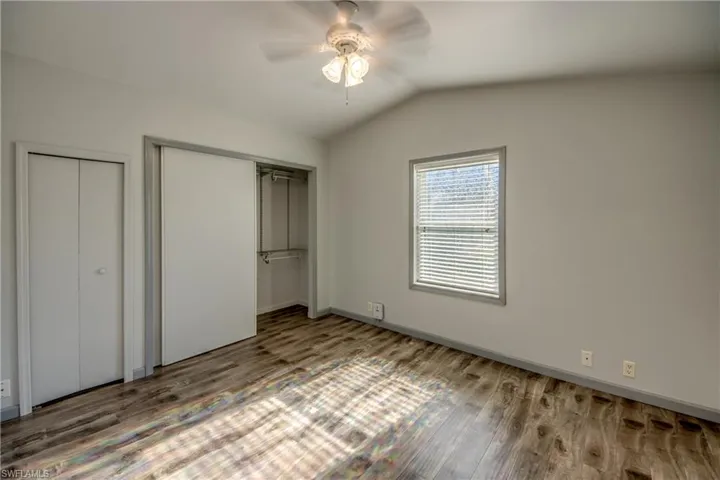 This room features a ceiling fan, hardwood style flooring, a window with blinds, and a closet with a sliding door and hanging rod