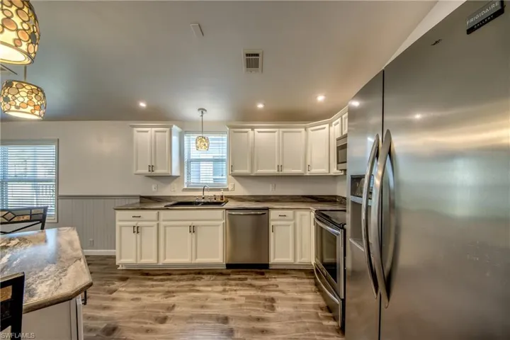 The kitchen features white cabinetry, stainless steel appliances, and wood-look flooring