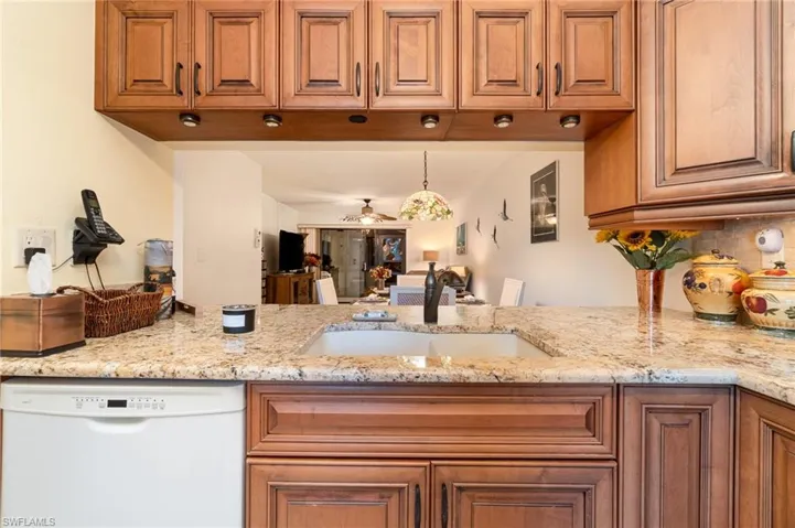 Kitchen with light stone countertops, ceiling fan, dishwasher, hanging light fixtures, and sink