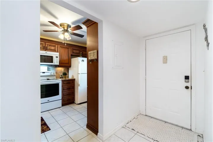 Kitchen with backsplash, white appliances, ceiling fan, light tile patterned floors, and electric panel