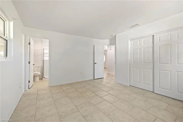 Unfurnished bedroom with a closet, visible vents, baseboards, ensuite bath, and light tile patterned floors