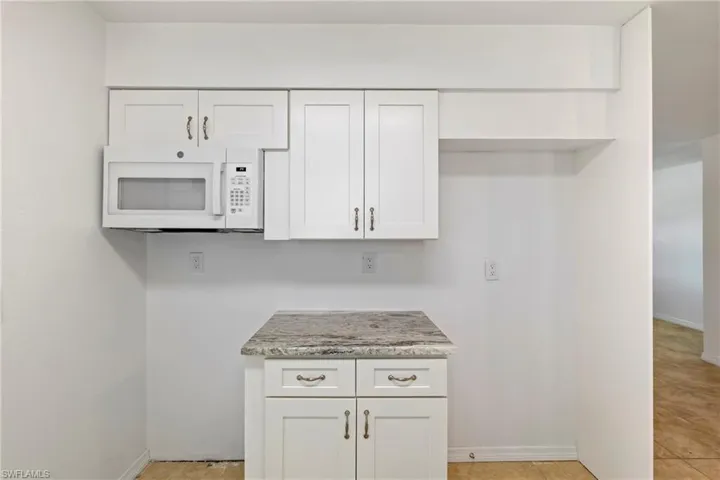 Kitchen featuring baseboards, white cabinets, and white microwave