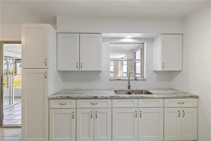 Kitchen featuring tasteful backsplash, light tile patterned floors, a sink, white cabinets, and light stone countertops