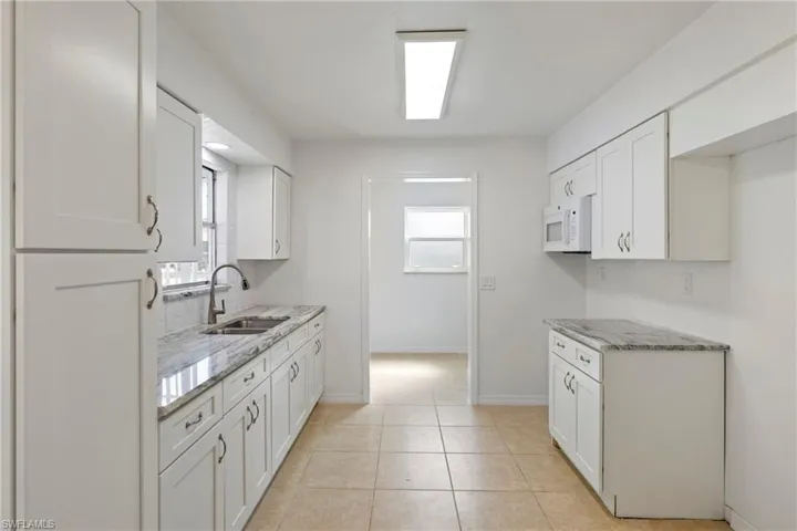 Kitchen featuring light stone counters, a sink, light tile patterned floors, white cabinets, and white microwave