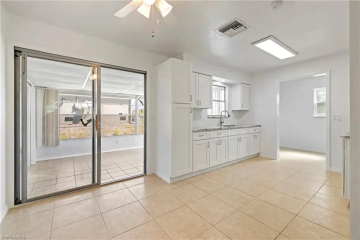 Kitchen with light tile patterned flooring, white cabinets, visible vents, a sink, and backsplash