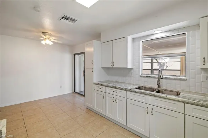 Kitchen with a sink, white cabinetry, tasteful backsplash, visible vents, and ceiling fan
