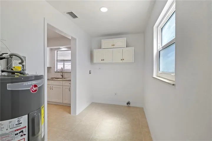 Clothes washing area featuring water heater, a sink, baseboards, visible vents, and cabinet space