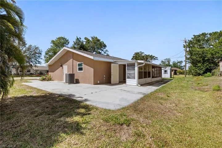 Rear view of property with a sunroom, a lawn, stucco siding, and a patio